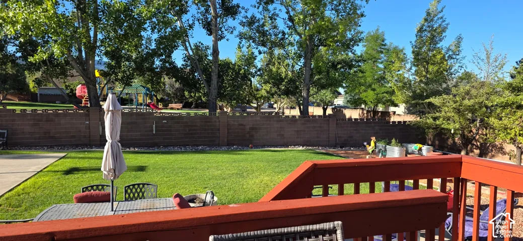 Backyard featuring a red-painted wood deck, expansive lawn, mature trees, and a masonry perimeter wall