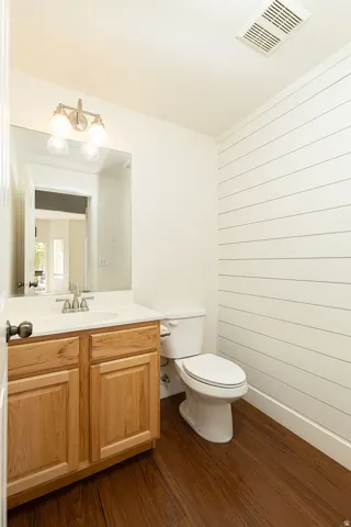 Wood-finish flooring with a white vanity featuring a ceramic sink, brushed nickel faucet, and a wall-mounted light fixture