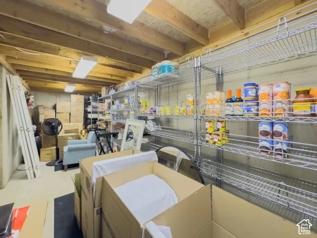Unfinished lower level featuring exposed wood beam ceiling, concrete walls, and overhead fluorescent lighting