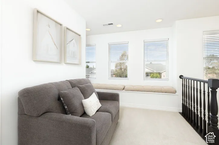 Recessed lighting, multiple windows with blinds, built-in window bench, light-toned carpeting, and dark wood-finish railing