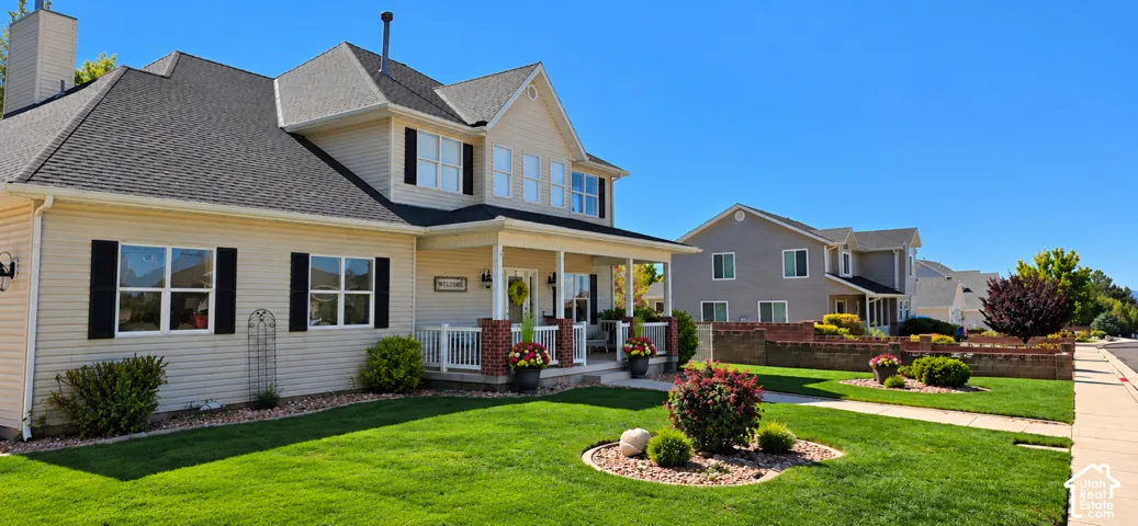 Two-story residence featuring light-toned horizontal siding, dark contrast shutters, a covered front porch with brick column bases, and a multi-gabled roofline
