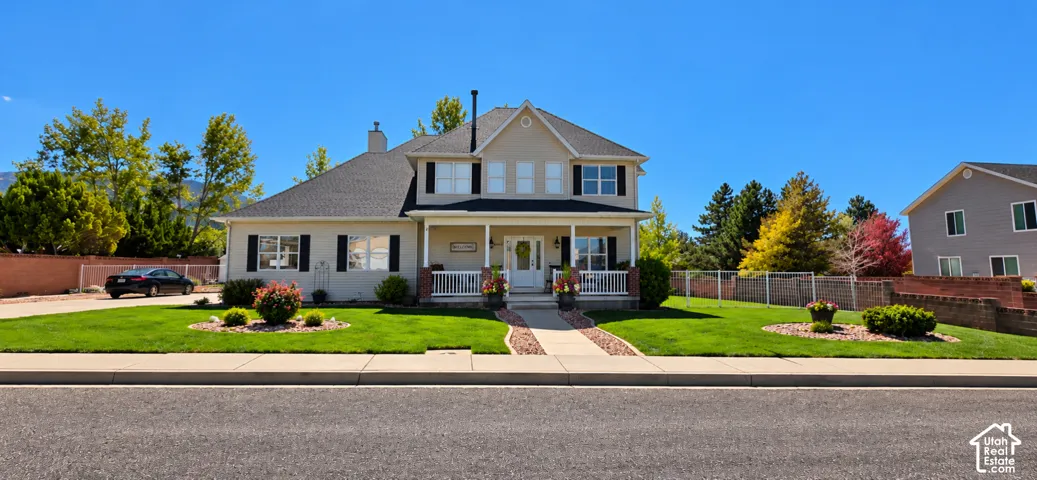 Two-story residence featuring a covered front porch, light-toned siding, dark shutters, and a shingled roof, set upon a landscaped lot with a stone-lined walkway
