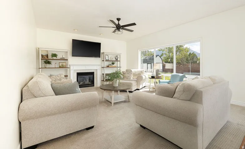 Living area with a built-in fireplace, a ceiling fan with integrated lighting, and a large window overlooking the outdoor space