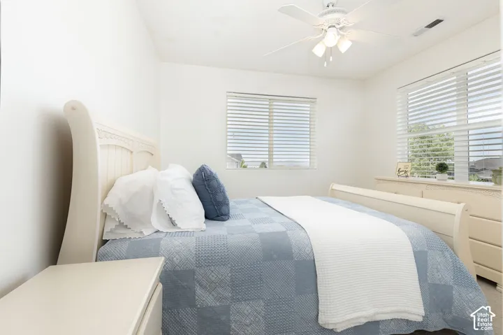 Bright room with two windows featuring white blinds, a ceiling fan with integrated lighting, and neutral carpeting