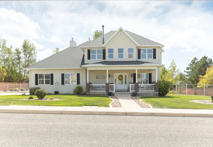 Traditional-style facade with light-colored siding, black shutters, and a covered front porch featuring white railings and brick accents