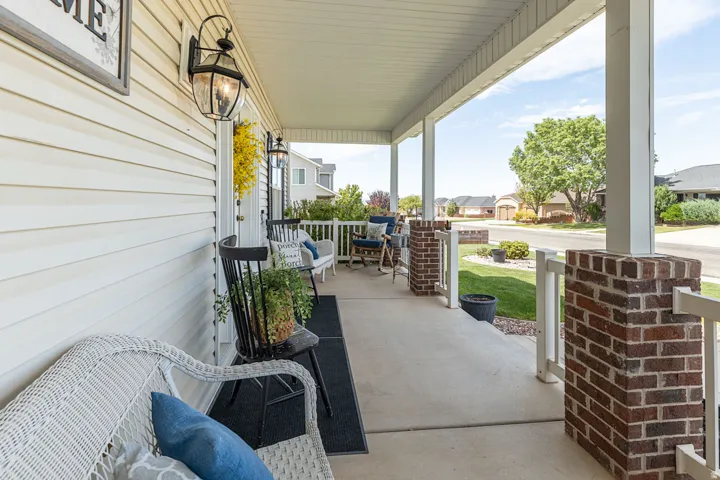 Spacious covered front porch with a concrete surface, white siding, brick pillars, and exterior wall lanterns