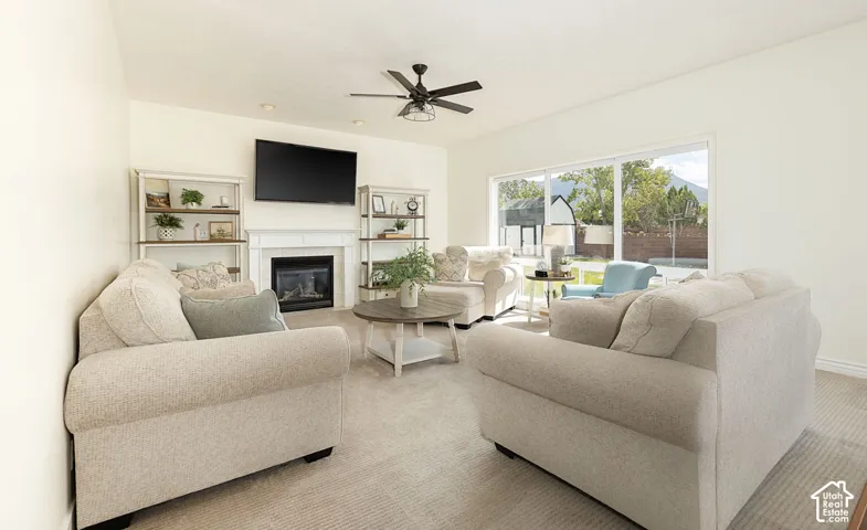 Living area with a built-in fireplace, a ceiling fan with integrated lighting, and a large window overlooking the outdoor space