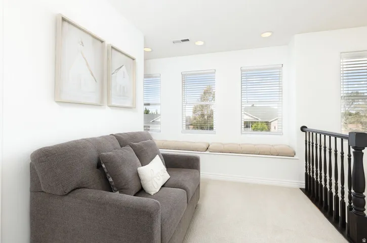 Recessed lighting, multiple windows with blinds, built-in window bench, light-toned carpeting, and dark wood-finish railing