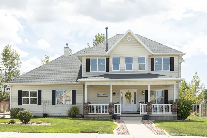Two-story residence featuring light-colored siding, a covered front porch with white railings, and brick accents