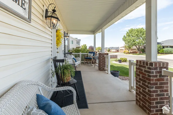 Spacious covered front porch with a concrete surface, white siding, brick pillars, and exterior wall lanterns