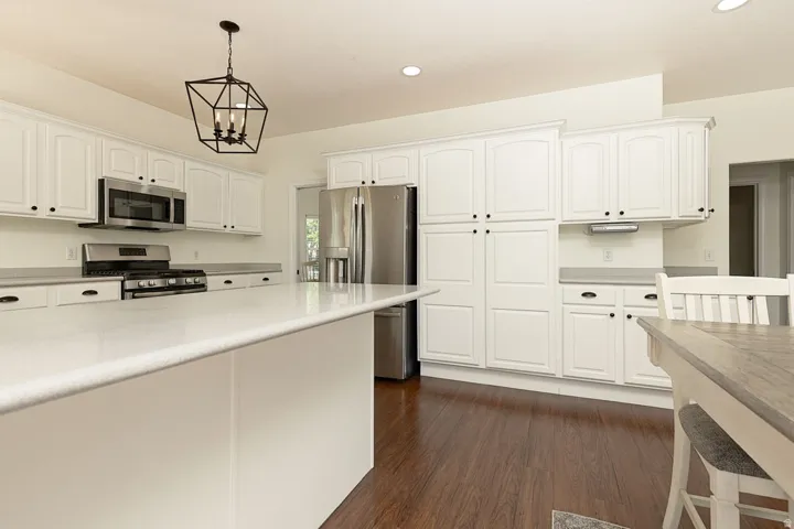 White cabinetry with black hardware, stainless steel appliances, extensive countertop space, wood-finish flooring, and a contemporary light fixture