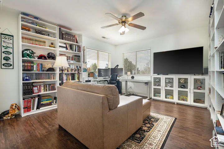 Dark wood-finish flooring with white built-in shelving, a ceiling fan with integrated lighting, and multiple windows with horizontal blinds