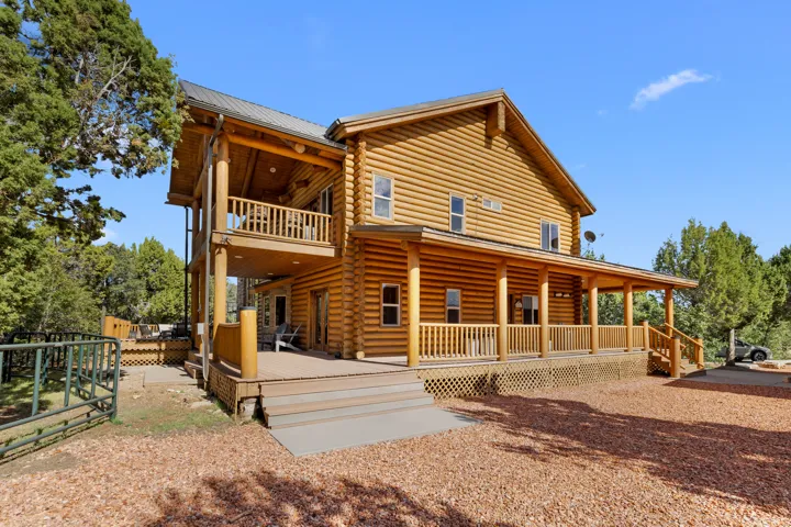 Log cabin exterior with a full-length covered porch, an upper-level balcony, a metal roof, and a multi-level deck