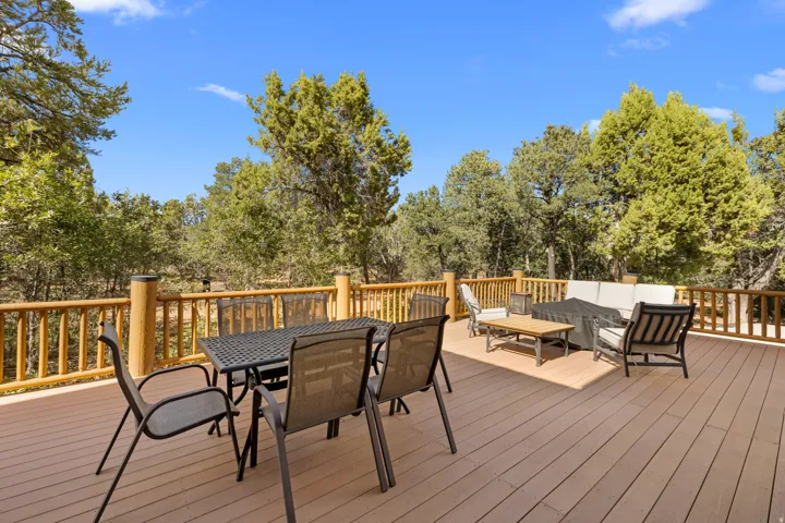 Expansive outdoor deck featuring wood-finish flooring, natural wood railings, and mature trees surrounding the property