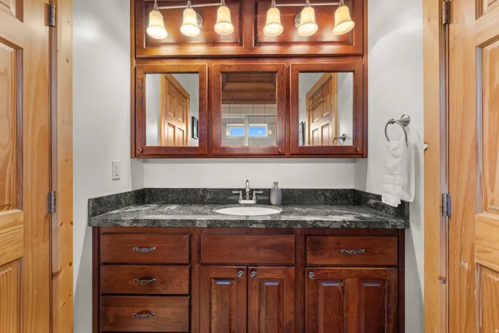 Jack and Jill bathroom with wood-finish vanity, a built-in sink, dark stone countertop, and upper cabinetry with integrated mirror panels