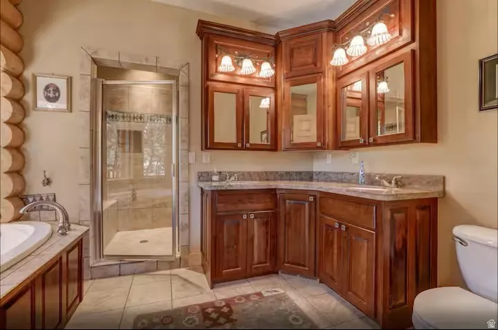 Primary bathroom with corner vanity and dual integrated sinks, wood cabinetry, and overhead mirrored storage