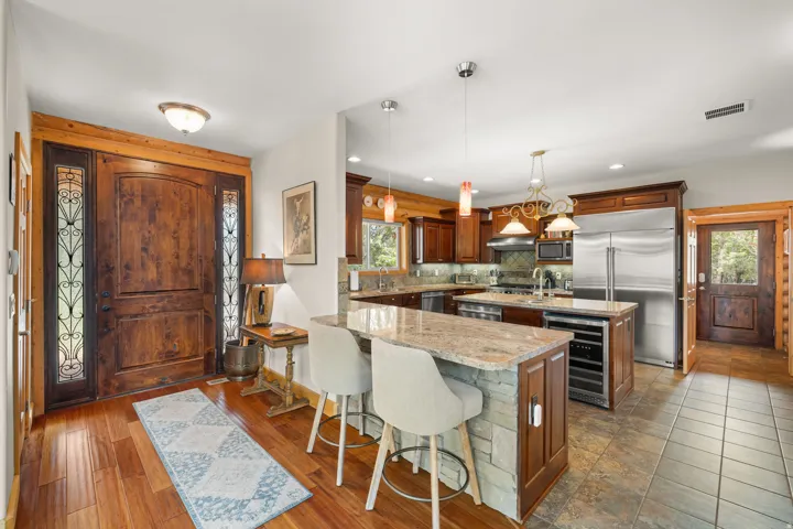 Wood-finish flooring, solid wood entry door with decorative glass side panels, kitchen with stainless steel appliances, kitchen island with stone-finish base, and recessed lighting