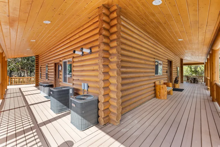 Expansive log home exterior featuring a wrap-around composite deck, log siding, and a wood-paneled ceiling with recessed lighting