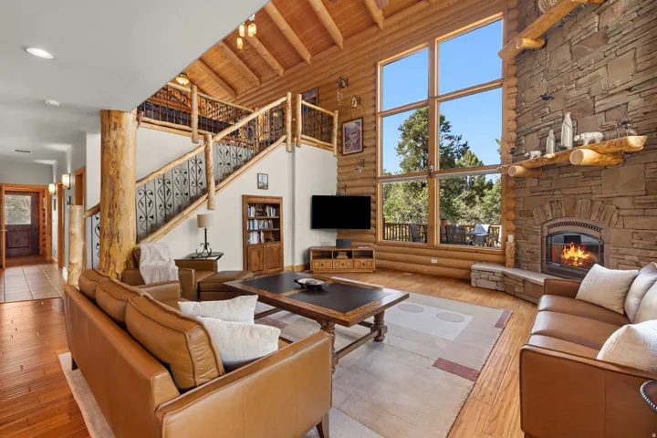 Two-story stone fireplace, large picture windows, wood-finish flooring, exposed log beams, and a decorative wrought iron staircase