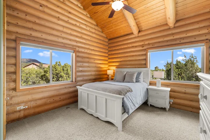 Bedroom 2 with vaulted wood-paneled ceiling and exposed beams, wood-plank walls, and two large windows