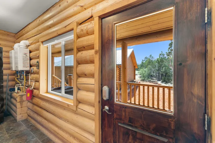 Log wall construction, wood-finish exterior door with glass insert, white frame window, and tile flooring