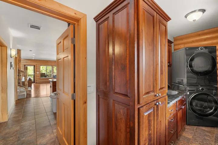 Wood-finish cabinetry with silver hardware, stacked front-load laundry appliances, granite-style countertop, and a built-in sink