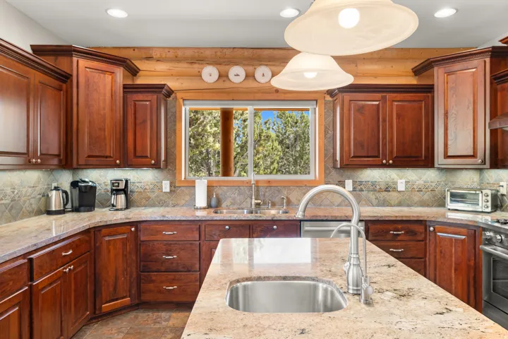 Wood-finish cabinetry, stone countertops, stone tile backsplash, recessed lighting, and a stainless steel sink
