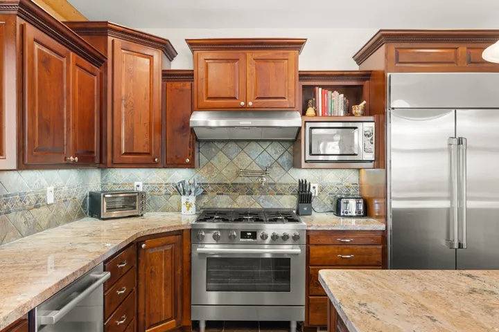 Rich wood cabinetry, stainless steel appliances, tile backsplash, and stone countertops