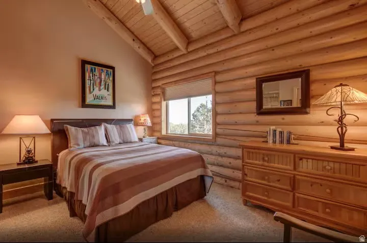 Bedroom 4 with vaulted wood-paneled ceiling, exposed log wall, window with horizontal blinds, built-in wooden dresser, and carpeted flooring