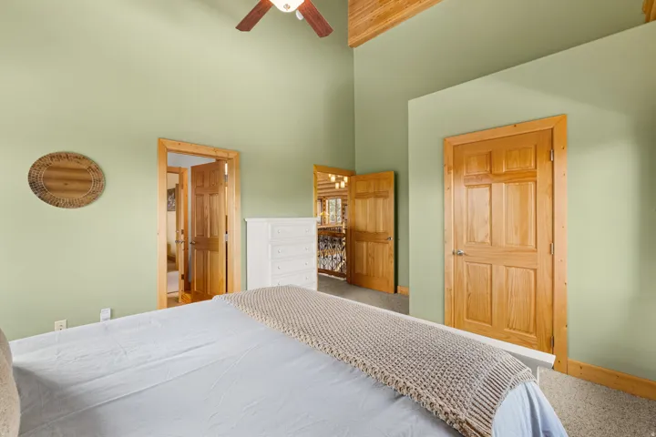 Bedroom 2 with vaulted ceiling and exposed wood beams, wood-paneled doors, wood trim, and a ceiling fan