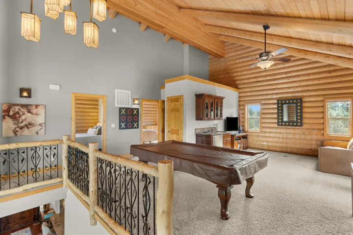 Vaulted wood-plank ceilings with exposed beams, wood-paneled walls, built-in wet bar, and a ceiling fan