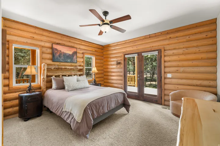 Log wall construction, dual pane windows, wood-finish ceiling fan, and glass-panel double doors in primary bedroom