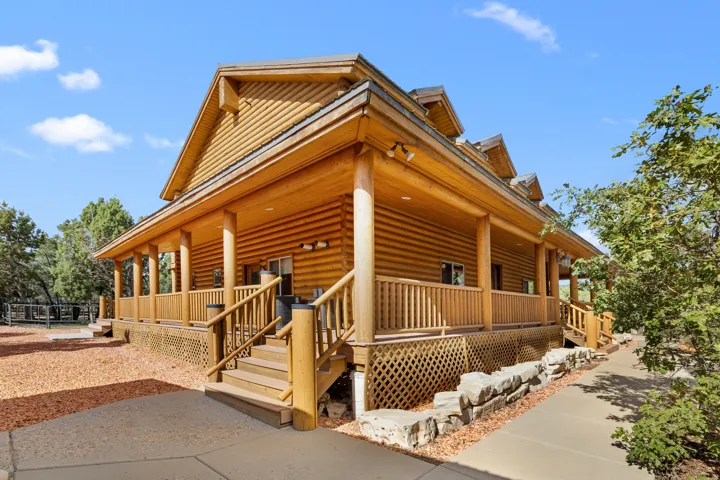 Log cabin exterior featuring a covered wrap-around porch, multiple windows, and a stone retaining wall