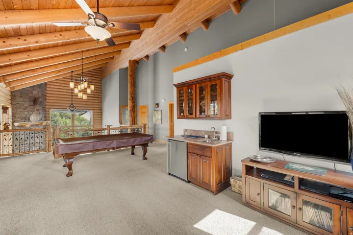 Vaulted wood-plank ceilings with exposed beams, built-in wet bar with cabinetry, stone fireplace, and log construction accents