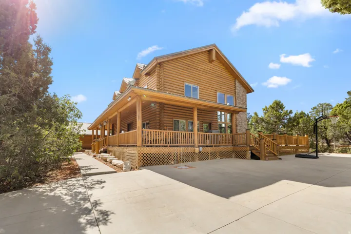 Log-style exterior featuring a covered porch, stone chimney, and multiple windows