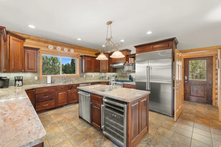 Kitchen featuring wood cabinetry, stainless steel appliances, a center island with under-counter wine refrigeration, granite countertops, and tile flooring