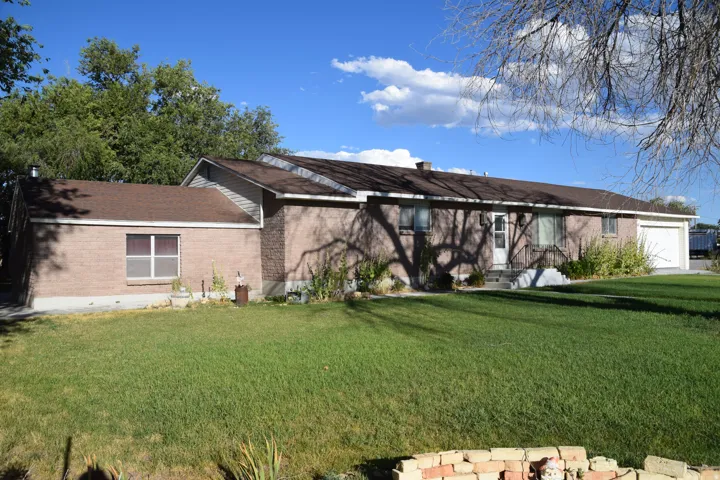 Brick exterior with an attached garage, featuring a front lawn and mature trees