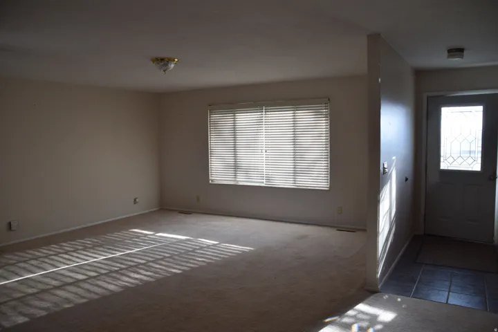 Carpeted flooring, window with horizontal blinds, ceiling-mounted light fixture, tile flooring at entry, and front door with decorative glass insert