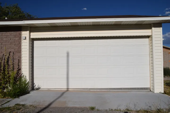 Single-panel garage door with horizontal paneling, light-toned siding, and a brick-finish exterior
