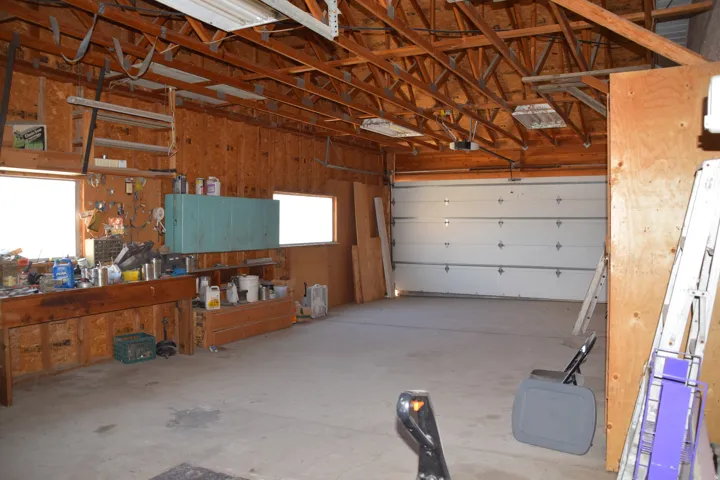 Exposed wood ceiling beams, concrete flooring, wood-paneled walls, built-in workbench, and overhead garage door