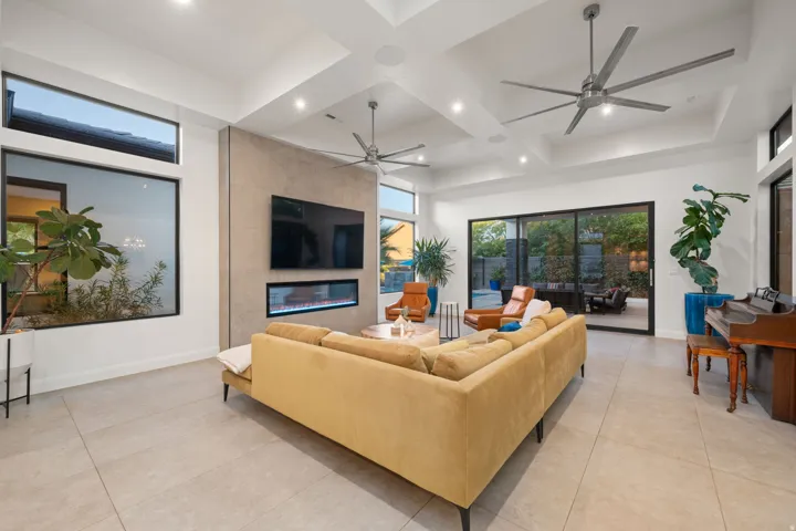 Expansive tiled flooring throughout, featuring a linear electric fireplace, contemporary ceiling fans, and a tray ceiling design