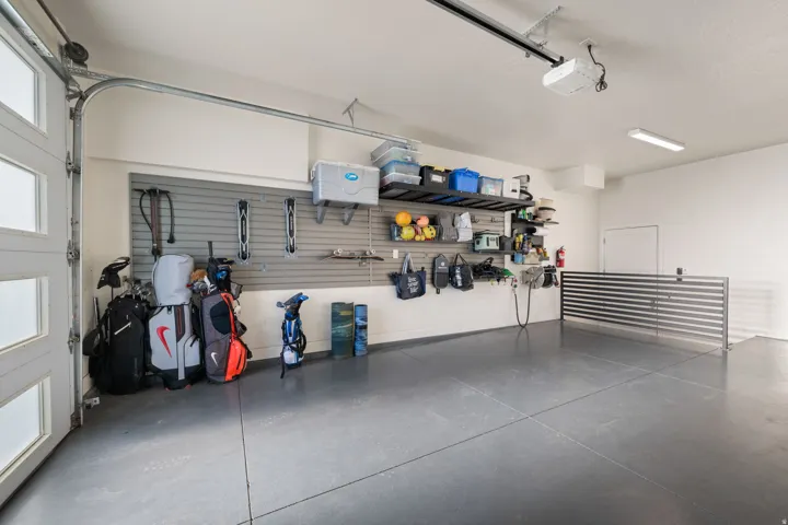 Garage with an overhead door featuring frosted window panels, wall-mounted storage organization, overhead lighting, and a painted concrete floor