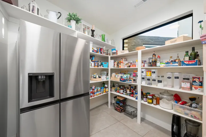 Stainless steel side-by-side refrigerator, extensive built-in shelving, high-level horizontal window, and neutral tile flooring