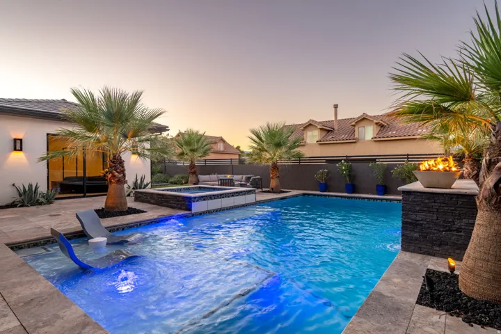 Resort-style pool with integrated spa and underwater lighting, surrounded by a stone paver patio and mature palm trees