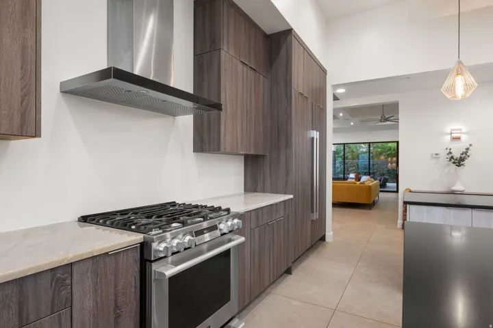 Gourmet kitchen featuring stainless steel appliances, wood-finish cabinetry, light-toned countertops, and a contemporary range hood