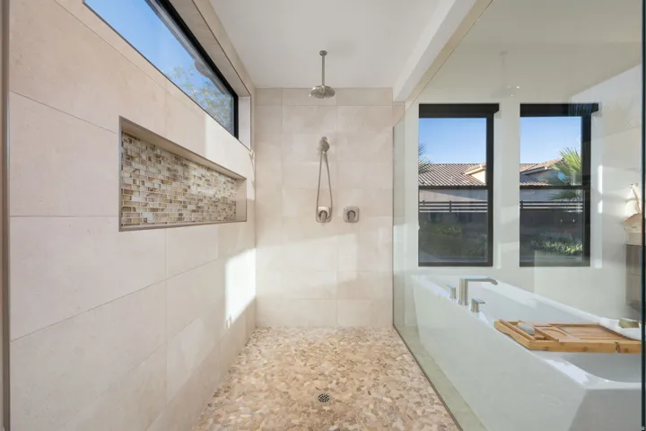 Glass-enclosed shower with pebble flooring, tiled walls, and a tiled shower niche