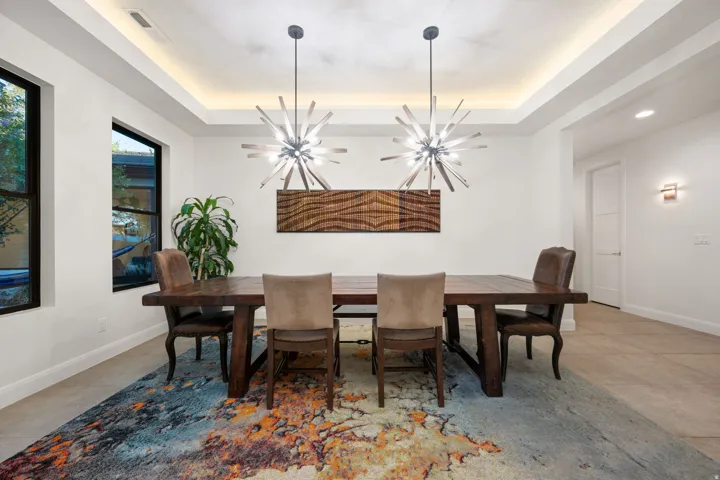 Tray ceiling with recessed lighting, two contemporary chandeliers, and two large windows