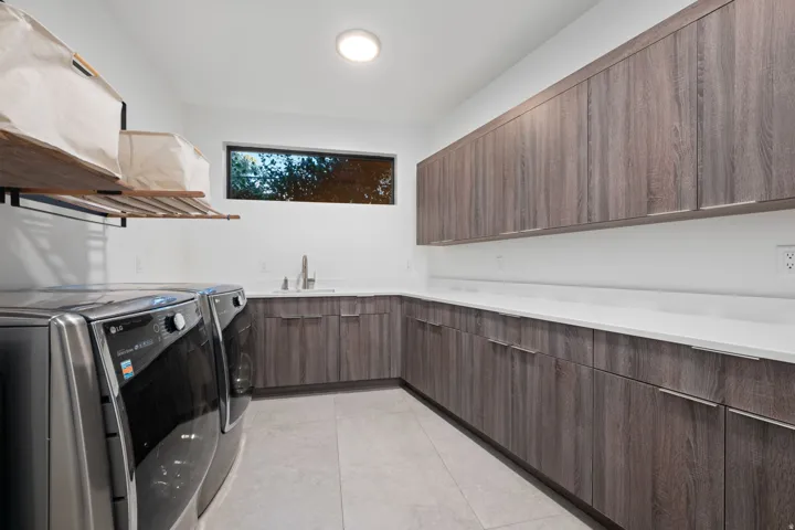 Expansive utility room featuring wood-finish cabinetry, light-toned countertops, integrated sink, and a rectangular window