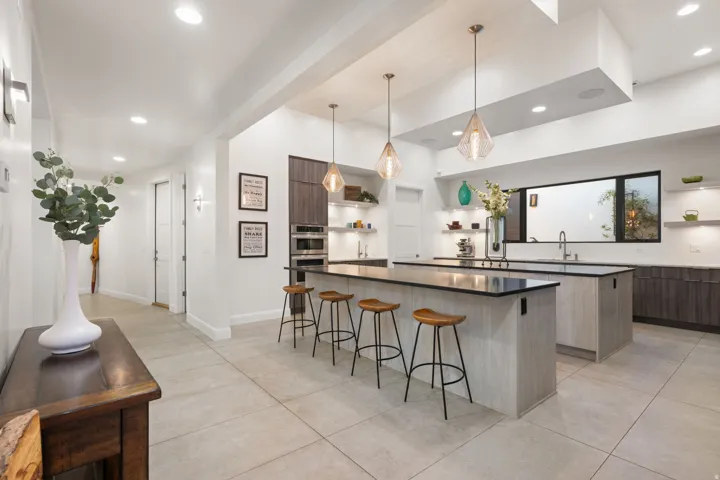 Spacious kitchen featuring two islands with black countertops, integrated double ovens, and a large window above the sink