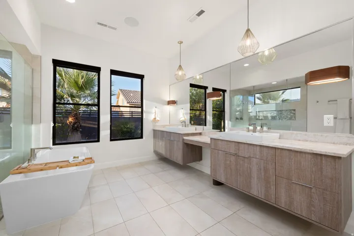 Contemporary bathroom with a freestanding soaking tub, dual floating vanities with surface-mount sinks, a full-wall mirror, and pendant lighting